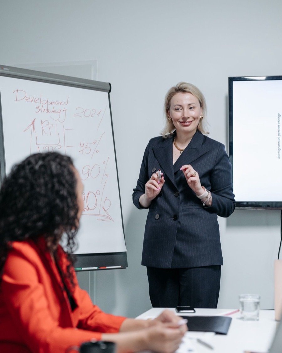 Une formatrice devant un paperboard, face à une participante qui prend des notes